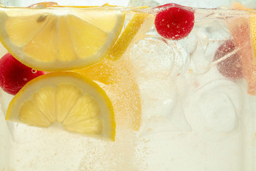 Close up of lemon slices and cherry in lemonade and ice cubes background. Texture of cooling sweet summer's drink with macro bubbles on the glass wall. Fizzing or floating up to top of surface. - obrazy, fototapety, plakaty