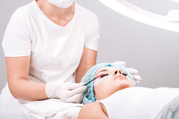 Obraz na płótnie Canvas eyelash master brushing false eyelashes on model face during procedure isolated on grey