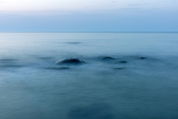 long exposure smooth sea surface with large stones sticking out of the water in blue twilight