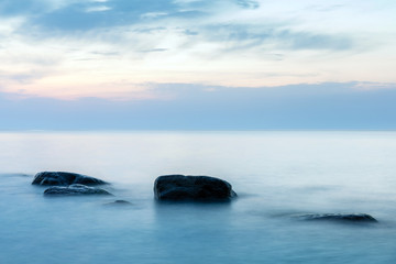 long exposure smooth sea surface with large stones sticking out of the water in blue twilight
