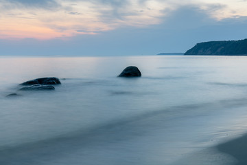 steep coastline on the horizon, long exposure smooth sea surface with large rocks sticking out of the water in blue twilight