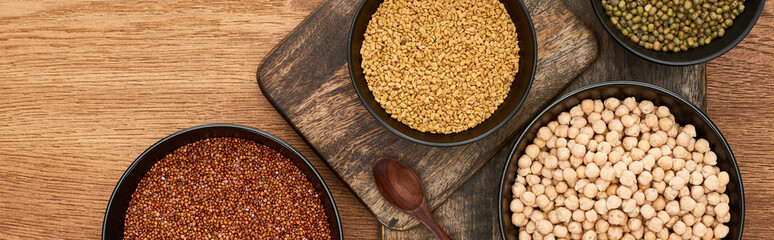 panoramic shot of bowls with roasted buckwheat, chickpea and beans near wooden spoon on wooden cutting boards