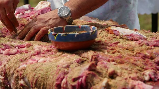 Farmer seasoning a whole lamb with a mix of herbs and salt before drying the meat 