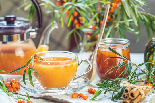 Hot spicy tea with sea buckthorn in glass cup and teapot, selective focus, rustic light background