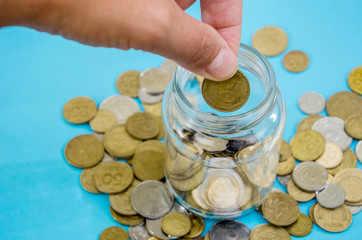 female hand throws a coin in a jar on a blue background. Close-up.