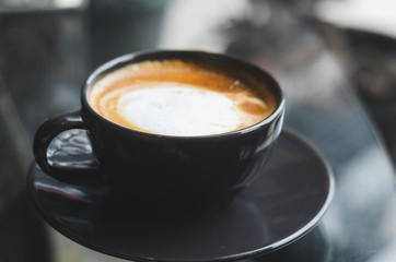 close up modern hot black coffee the cappuccino on dark background with coffee bubble foam pattern and texture in black cup looking and feel so delicious on glasses table in coffee shop.