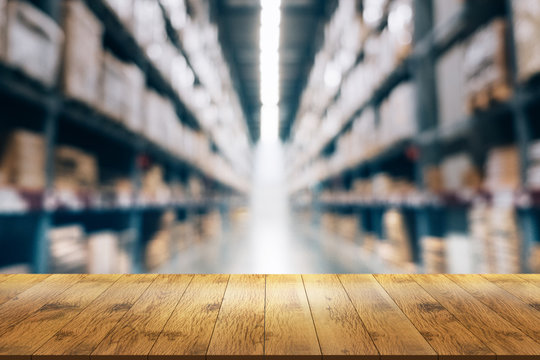 Empty wooden table in front with blurred background of warehouse storage.