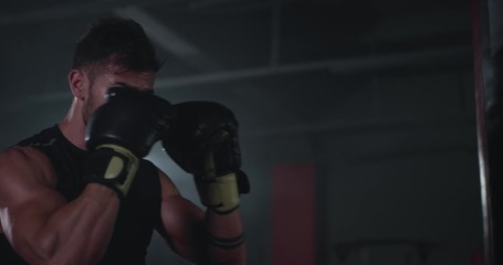 In a large boxing class young attractive guy with perfect muscle boxing hard in a punching bag