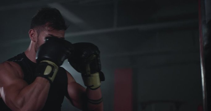 In a large boxing class young attractive guy with perfect muscle boxing hard in a punching bag