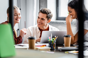 multiethnic students smiling and looking at laptop in apartment
