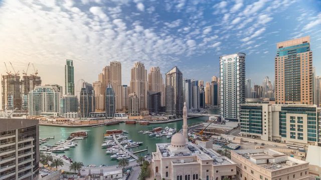 Yachts in Dubai Marina flanked by the Al Rahim Mosque and residential towers and skyscrapers aerial timelapse. Modern high rise skyline with boats and wooden dhows