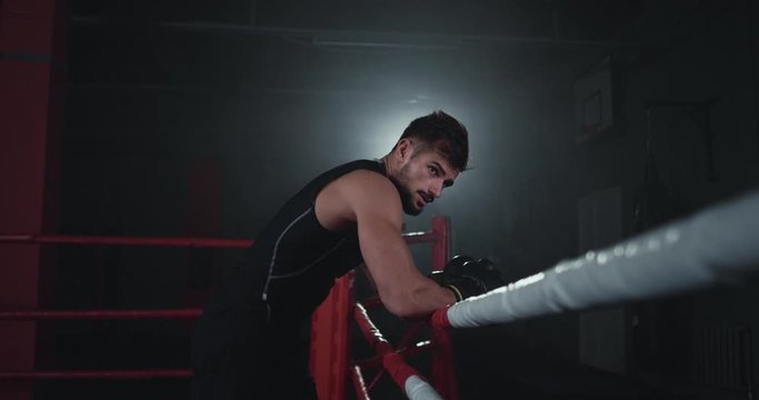 In a dark boxing ring attractive strong fit body guy have a break after a intense workout training