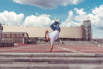 Male athlete, guy dancer summer city. Standing one arm jump. Fashionable modern break dance style fast, fitness sport hip hop motion. Urban culture street dance. Acrobatic exercises. In t-shirt jeans.