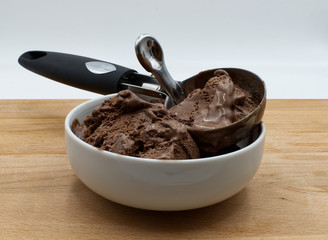Chocolate ice cream for dessert, spoon for ice cream in a white jar, wooden table, white background