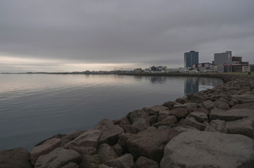 Seascape with stone coast in reykjavik, iceland. City building on sea side. Skyline on cloudy sky. Architecture and construction. Early morning, mooody sky.