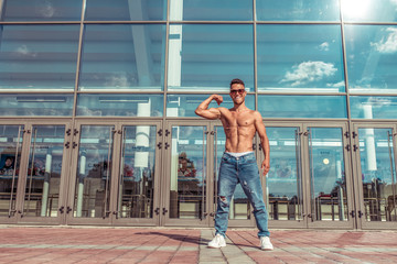Man athlete, guy dancer summer city. Glasses background glass windows. Tanned inflated torso abs and biceps. Fashionable modern break dance style, fitness sport hip hop. Urban culture, street dance.
