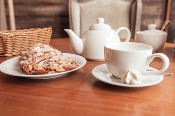 White cup, tea pot and croissant on table in cafe