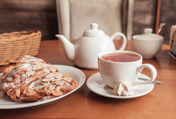 Tea cup, teapot and croissant on table in cafe
