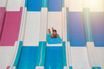 Summer fun in water park. Cute boy sliding down the slide on colorful inflatable floater.  He is on...