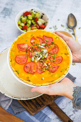 Hands holds pumpkin veggie casserole  with tomatoes and herbs. Vegan food and vegetarian lunch.
