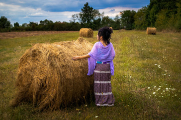 Naklejka na ściany i meble Woman on a meadow with hay bale at sunset