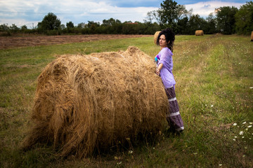 Naklejka na ściany i meble Woman on a meadow with hay bale at sunset