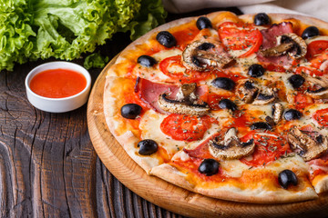 Pizza with tomato, olives, champignons, ham and cheese on round wooden plate