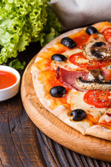 Pizza with tomato, olives, champignons, ham and cheese on round wooden plate