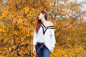 Red-haired girl in a white sweater posing in the autumn forest