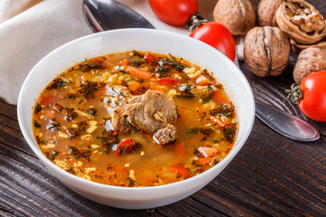 Georgian soup. Kharcho with rice, tomato, beef, garlic and herbs in bowl on wooden table
