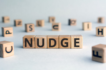 Nudge - word from wooden blocks with letters, pushing gently concept, random letters around, white ...