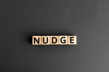 Nudge - word from wooden blocks with letters, pushing gently concept, random letters around, top...