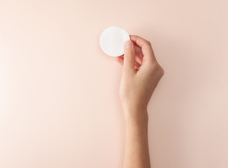 Cotton pad in the female right hand on a pink background
