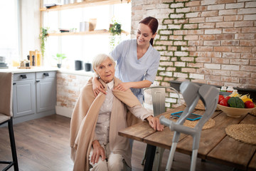 Caring nurse putting plaid on shoulders of aged woman