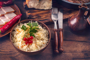 Ukrainian national cuisine - sauerkraut, donuts with garlic, fork, knife, small jug, lard and spicy pepper on a plate on a dark wooden background. Processing photos with tinted.