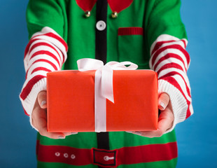 Santa's little helper holding holiday gift with ribbon on background