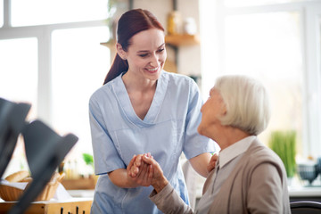 Red-haired caregiver smiling and talking to aged woman - obrazy, fototapety, plakaty