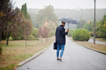 Fashionable tall arab beard man wear on black coat with umbrella and bag case posed at rain weather day.