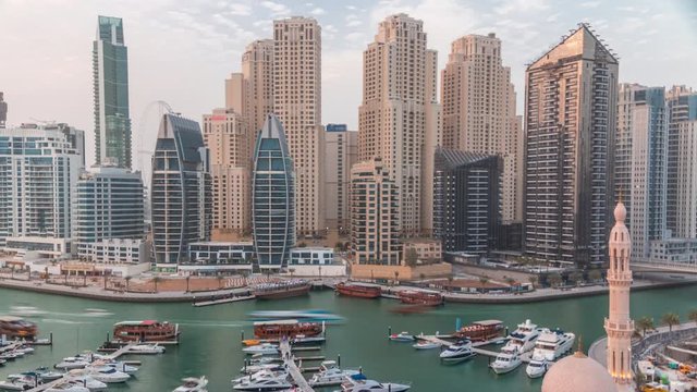Yachts in Dubai Marina flanked by the Al Rahim Mosque and residential towers and skyscrapers aerial timelapse. Modern high rise skyline with boats and wooden dhows