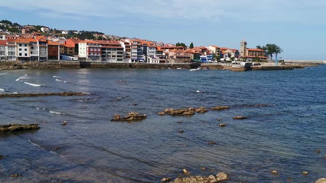 Village on the coast of the Cantabrian Sea. The church tower at one end, moored boats and people bathing in the sea. Luanco Asturias. Spain