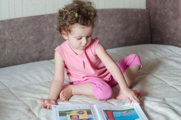 Cute girl reading book at home. the clever child is considering interesting pictures.