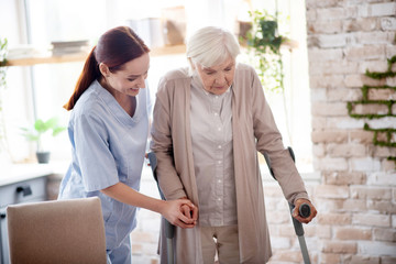 Helpful caregiver assisting woman with crutches