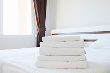 Hotel room with freshly made bed, perfectly clean and ironed sheets, stack of new folded towels in natural sun light. Close up, copy space for text.