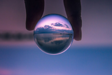 Sunset seen in a crystal ball. Jetty on a quiet beach with clouds and blue sky