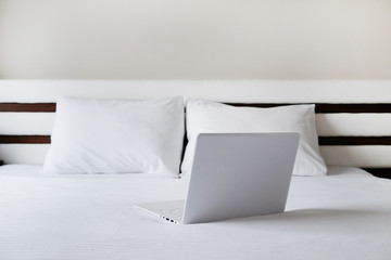 Hotel room with freshly made bed, perfectly clean and ironed sheets, laptop computer in natural sun light. Close up, copy space for text.