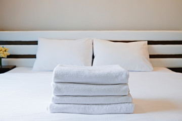 Hotel room with freshly made bed, perfectly clean and ironed snow white sheets, stack of new folded towels in natural sun light. Close up, copy space for text.
