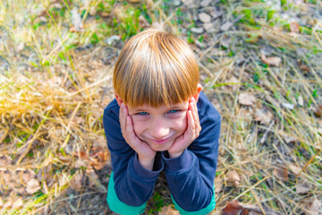 The boy squats on the grass, propping his head in his hands and looking at the top in the camera,...