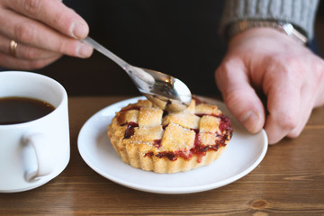 man in grey sweater drinks black lungo americano coffee in winter autumn in coffee shop eating classic american home-made cherry pie on white plate on wooden table. Fall mood instagram style