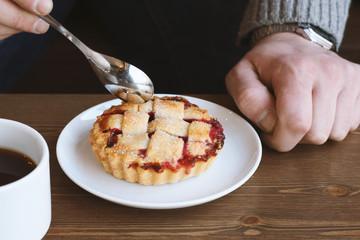 man in grey sweater drinks black lungo americano coffee in winter autumn in coffee shop eating classic american home-made cherry pie on white plate on wooden table. Fall mood instagram style