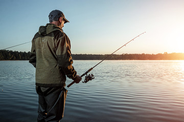 Male fisherman at dawn on the lake catches a fishing rod. Fishing hobby vacation concept. Copy...